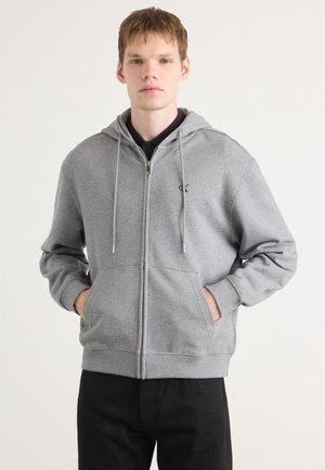 Grijze zip-up hoodie van zachte stof, met een voorzak, verstelbare trekkoordkap en een klein logo op de linkerkant van de borst.