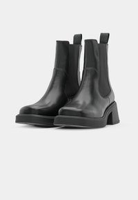 Svarta läderankelstövlar med elastiska sidopaneler, en böjd klack och en slät yta. Designen har en minimalistisk stil.