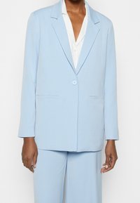 Blazer azul claro con un corte relajado, cierre de un solo botón, solapas con muesca y dos bolsillos laterales, hecho de una tela suave.