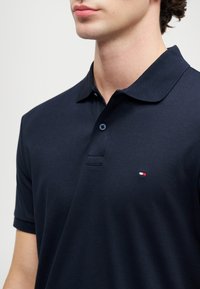 Námořnická modrá polo košile vyrobená z měkké bavlny. Obsahuje klasický límec, tři knoflíky a malé vyšívané logo na hrudníku.