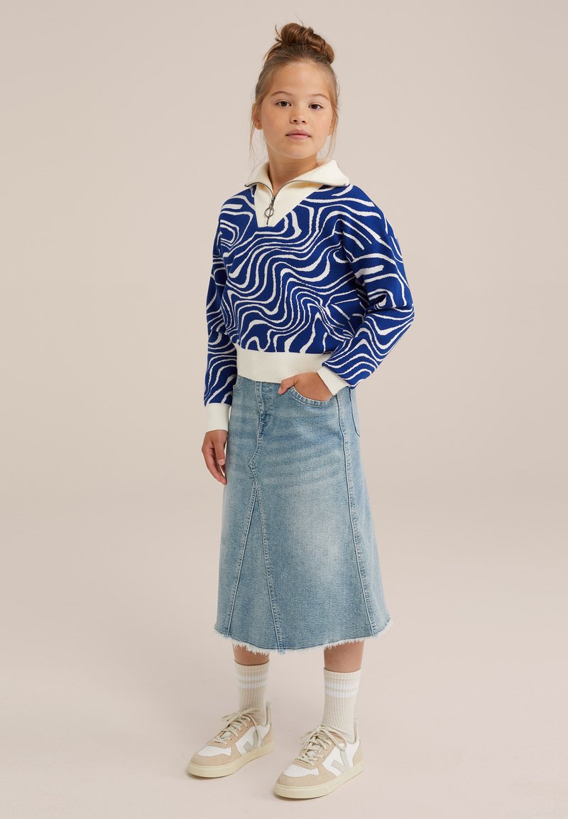 Kék és fehér mintázattal ellátott pulóver, cipzáros gallérral, világos farmer szoknyával, amelyen nyers szegély található, valamint semleges árnyalatú sportcipőkkel és zoknikkal párosítva.