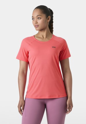 Žena s copánky, která má na sobě korálové sportovní tričko s krátkým rukávem a fialkové legíny, hledí vlevo na bílém pozadí.