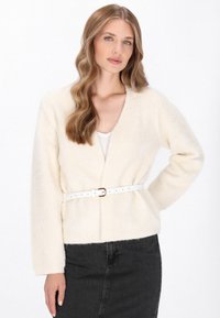 Cream-colored, fluffy cardigan with long sleeves and a V-neck. Features a white belt with a rectangular buckle, paired with a black skirt.