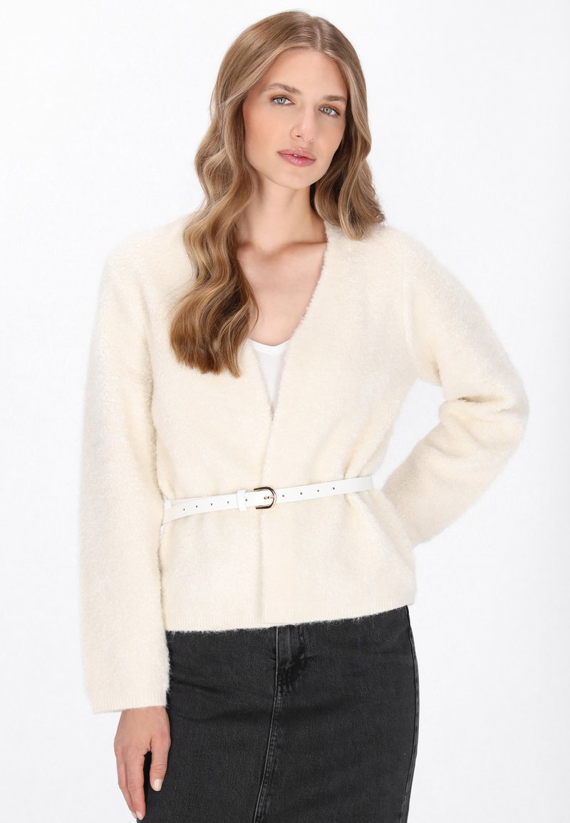 Cream-colored, fluffy cardigan with long sleeves and a V-neck. Features a white belt with a rectangular buckle, paired with a black skirt.