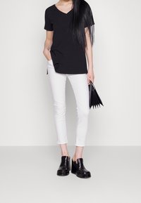 Camiseta negra de manga corta y cuello en V, pantalones blancos ajustados y zuecos negros de plataforma. Los accesorios incluyen un pequeño bolso negro con pliegues.
