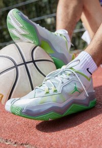 Basketbollskor i ljusgrått med gröna detaljer, med ett texturerat mesh-överkärl, dämpad sula och zigzag-mönster på yttersulan.