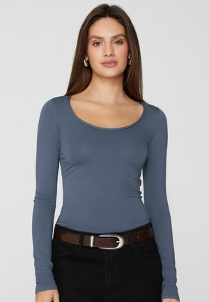 Haut ajusté à manches longues en tissu bleu doux avec un col rond, associé à une jupe foncée et une ceinture marron avec une boucle argentée.