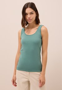 Top aderente color turchese realizzato in cotone morbido ed elastico con scollatura aU. Presenta spalline larghe e una consistenza liscia.