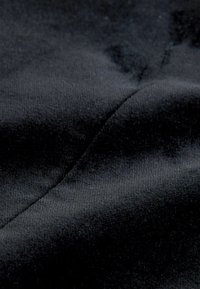 Fekete szövet, amely lágy tapintású, sima felületet és enyhe fényt mutat. Látható varrásokkal bír, ferde mintázatban.