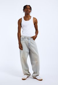 Biały top na ramiączkach, jasnoniebieskie oversize'owe dżinsy, białe trampki z beżowymi podeszwami, srebrny naszyjnik łańcuszkowy, na jednolitym białym tle.