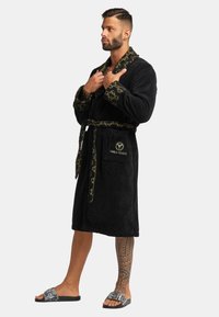 Black terry cloth robe with leopard print collar and cuffs, waist tie, and embroidered logo. Features a front pocket and stylish sandals.