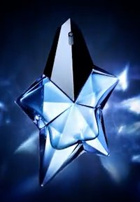 Bottiglia di profumo a forma di stella in vetro trasparente e blu chiaro, caratterizzata da sfaccettature angolari e un tappo a punta nera.