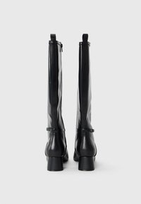 Botas altas pretas feitas de couro liso, com ponta arredondada, saltos em bloco e um fecho éclair na parte de trás. Design simples com mínimos acessórios.