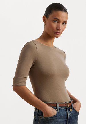 Beige aansluitend topje met driekwartmouwen, ronde halslijn en een gladde textuur, gecombineerd met hoge blauwe jeans en een bruine riem.