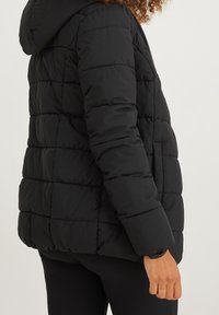 Chaqueta de plumas negra con capucha, con secciones acolchadas, cremallera frontal y puños elásticos para mayor calidez y estilo.