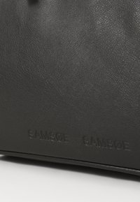 Černá kožená taška s texturovaným povrchem. Na spodní straně se nachází embosované logo "SAMSNØE", které ukazuje elegantní, minimalistický design.
