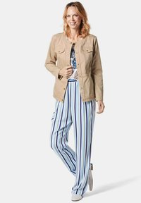 Lichtgewicht tan jack met drukknoopsluiting, gecombineerd met blauw-wit gestreepte, wijde broeken. De bovenkant heeft een bloemmotief in blauwe tinten.