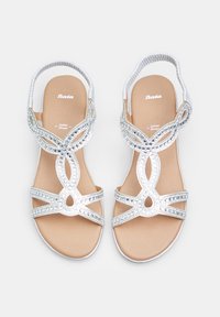 Sandales argentées avec des brides en tressé élaborées et des strass décoratifs, avec une semelle beige lisse et un design ouvert au niveau des orteils.