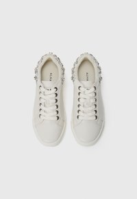 Baskets blanches avec une finition en cuir lisse, ornées d'un accent en strass le long du col, et dotées d'un système de laçage traditionnel.