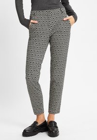 Schwarz-weiße gemusterte Hose mit einem Diamantdesign, mit seitlichen Taschen und schmal zulaufendem Bein. Hergestellt aus einem glatten Stoff.