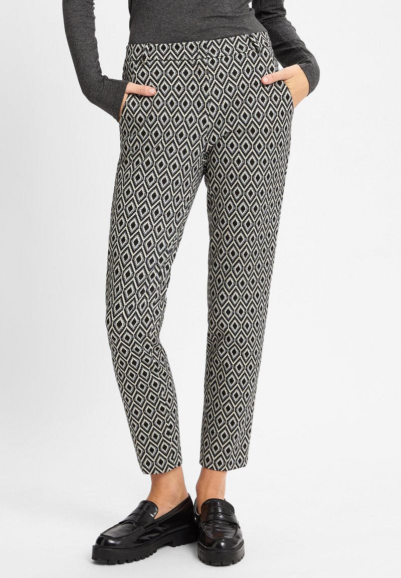 Schwarz-weiße gemusterte Hose mit einem Diamantdesign, mit seitlichen Taschen und schmal zulaufendem Bein. Hergestellt aus einem glatten Stoff.