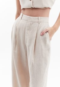 Beige linnen high-waisted broek met plooien, voorzien van zijzakken en een rechte pijp. Lichtgewicht en gestructureerde stof.