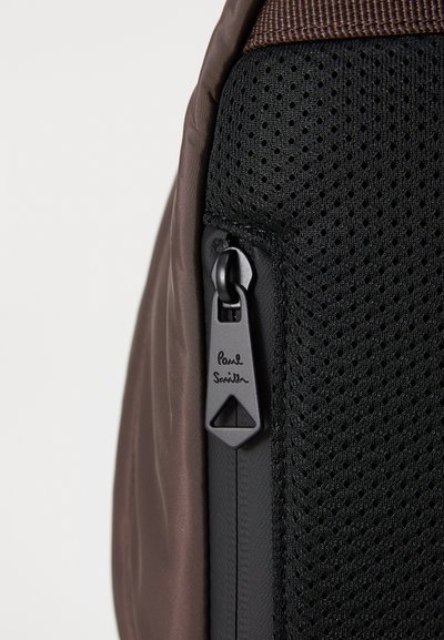Pruun nailonist seljakott, millel on tekstureeritud musta võrgupaneel, must tõmblukk, millel on "Paul Smith" brändi logo.