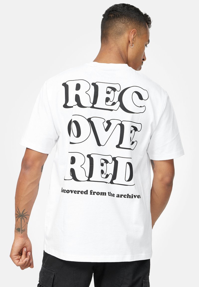 Hvid bomulds-T-shirt med fed sort tekst på ryggen: "GENVUNDET RØD," med "genvundet fra arkiverne" nedenfor i en mindre skrifttype.