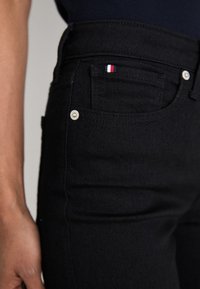 Sorte denim jeans med høy livhøyde, med sølvfarget beslag og et lite rødt, hvitt og blått logo-merke på frontlommen.