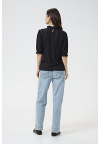 Blusa nera con maniche a palloncino e dettaglio a chiave sulla schiena, abbinata a jeans a vita alta di colore azzurro chiaro. Tessuto liscio con un motivo testurizzato.