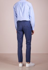 Jasnoniebieska koszula zapinana na guziki, granatowe dopasowane spodnie, białe trampki. Spodnie mają kieszenie z tyłu; koszula ma tradycyjny kołnierzyk i długie rękawy.