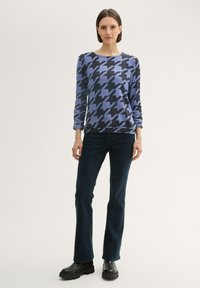 Blauer und schwarzer Hahnentritt-Muster Strickpullover mit langen Ärmeln, getragen mit dunkelblauen Schlagjeans und klobigen schwarzen Stiefeletten.