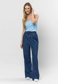 Pantaloni din denim cu un design cu picioare largi, de culoare albastru închis, și o talie elastică cu un șnur. Asortați cu un top fără mâneci de culoare albăstruie, cu textură rib bată, și pantofi albi.