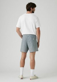Pantaloni corti a righe blu con una tasca posteriore, indossati con una maglietta bianca e calze bianche alla caviglia. Abbinati a scarpe beige con un design casual.