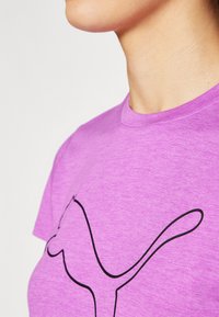 Camiseta de algodón morada con un gran logo negro contorneado en el frente, cuello redondo y mangas cortas.