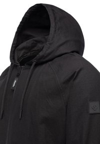 Svart huva jacka med dragkedja fram, texturerad tyg, justerbara dragsnören och en märkt gummipatch på vänster ärm.