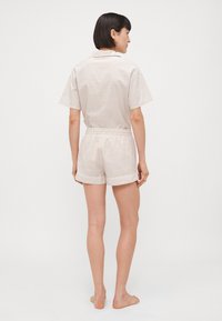 Lichtbeige pyjamastel met korte mouwen en een kraaghals, met een subtiel gestreept patroon, elastische tailleband en contrasterende afwerking.