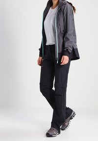 Voděodolná šedá bunda s světle modrými akcenty, v kombinaci s černými kalhotami a šedými turistickými botami. Obsahuje kapuci a kapsy na zip.