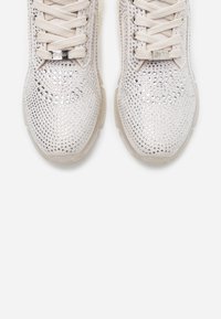 Baskets beige clair avec une tige texturée incrustée de strass argentés, bout rond et lacets plats. Semelle en caoutchouc transparent.