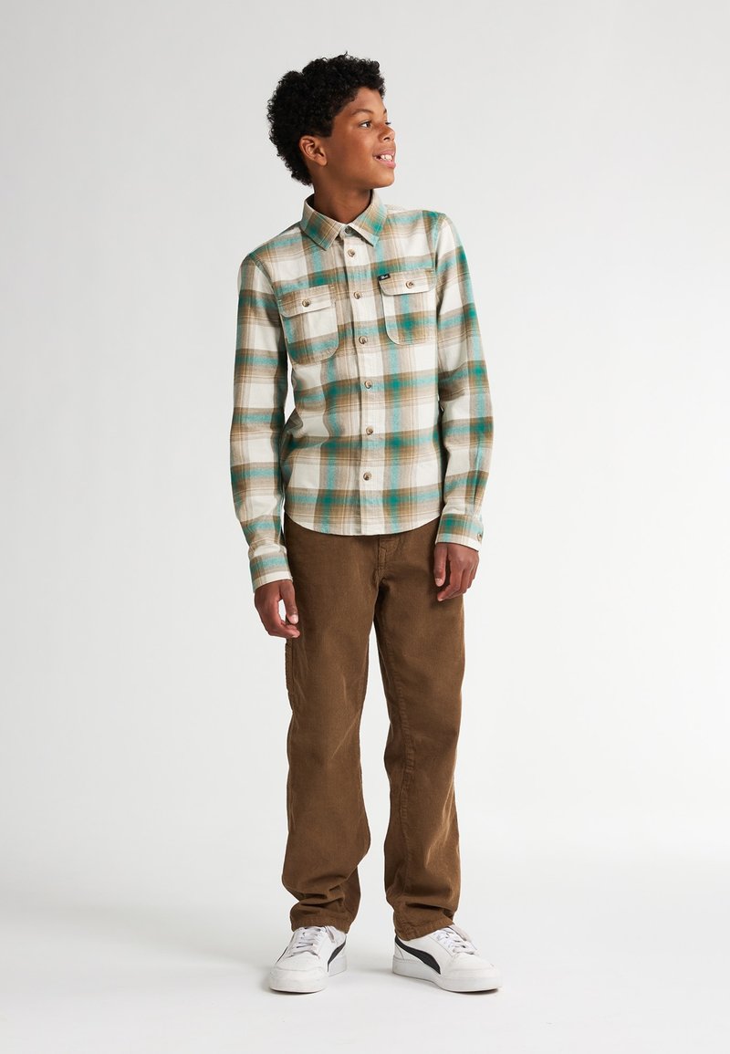 Kostkovaná košile v zelených, modrých a hnědých tónech s límečkem na knoflíky a dvěma předními kapsami, spárovaná s hnědými kordovým kalhotami a bílými teniskami.