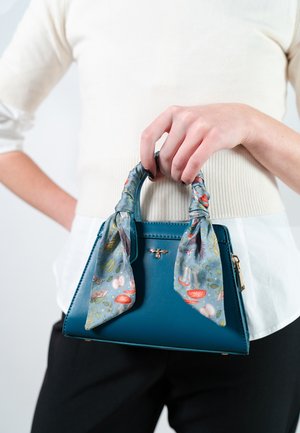 Taschenhandtasche aus tealfarbenem Leder mit strukturierter Form, versehen mit einem mit Blumenmotiven geschmückten Schal, der an den Griffen gebunden ist, und einem goldfarbenen Bienenemblem auf der Vorderseite.