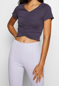 Lila, åtsittande crop top med korta ärmar, texturerad ruching fram och vågig nederkant. Matchad med ljuslila högmidjade byxor.