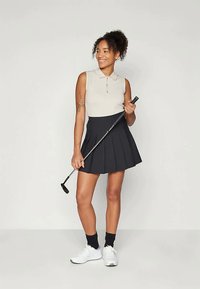 Μπεζ πόλο μπλούζα με γιακά, συνδυασμένη με μαύρη πλισέ φούστα γκόλφ. Λευκά αθλητικά παπούτσια και μια μπάλα γκόλφ που κρατείται με το ένα χέρι.