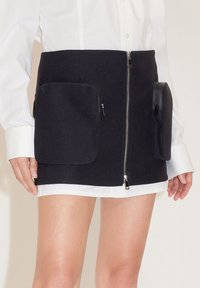 Zwarte wollen mix minirok met een voorkleur, twee zijzakken en een gladde textuur, gecombineerd met een witte blouse met lange mouwen.
