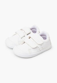 Białe trampki z dwoma paskami na rzep, gładką syntetyczną cholewką, gumową podeszwą, okrągłym noskiem oraz małymi perforacjami po bokach dla wentylacji.