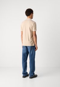Beige bomullspolo skjorte med korte ermer og hvite krageakenter, kombinert med løstsittende blå denim jeans og svarte sko.