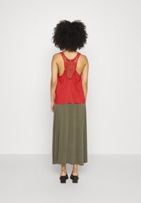 Top vermelho sem mangas com detalhes em renda nas costas, combinado com uma saia longa verde oliva e sapatos pretos de salto bloco.