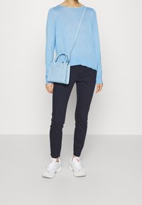 Suéter azul claro, pantalones navy oscuros y zapatillas blancas. La bolsa es pequeña, azul claro con un acabado texturizado y doble mango.