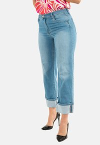 Jeans de mezclilla azul claro con corte recto, dobladillos enrollados y sutiles desgastes en los muslos. Combinados con tacones altos negros.