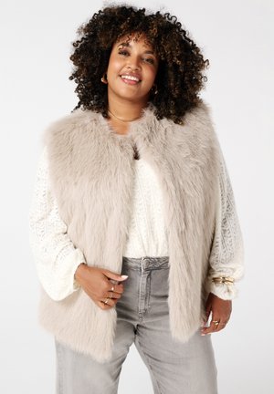 Nepbont vest in licht beige, met een zachte textuur, zonder sluiting, gelaagd over een crèmekleurig gebreid topje, gecombineerd met grijze broek.